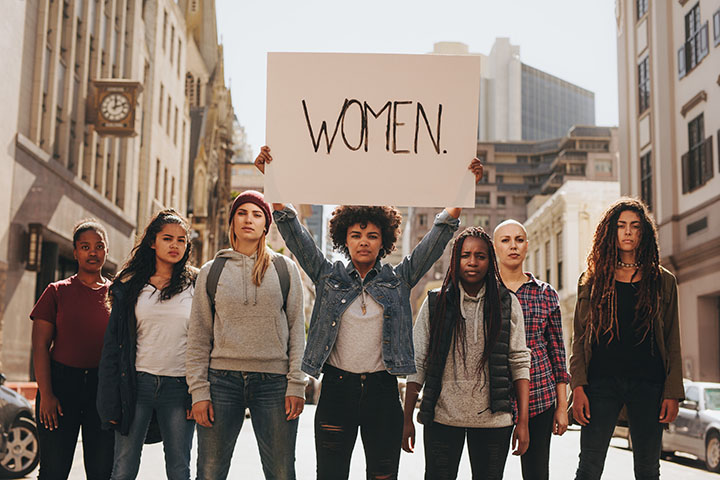 Group of women marching on the road in protest. Young woman holding a protest sign about women empowerment